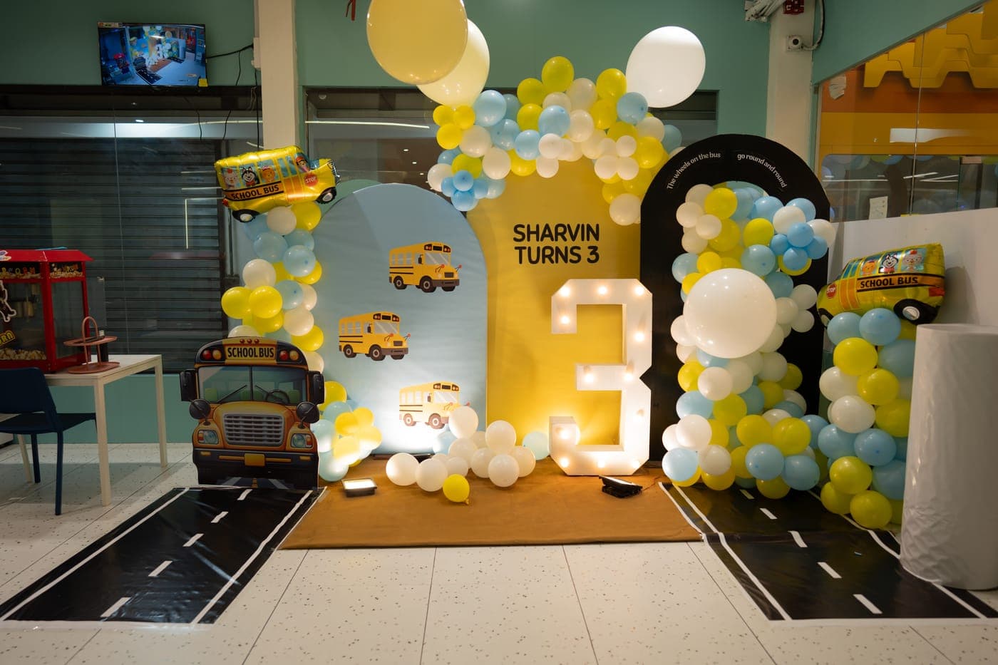 School-bus themed birthday setup with a glowing number 3 and balloon arches